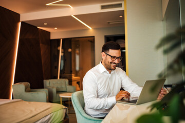 Elegant smiling man using laptop in the luxury hotel room, portrait.
