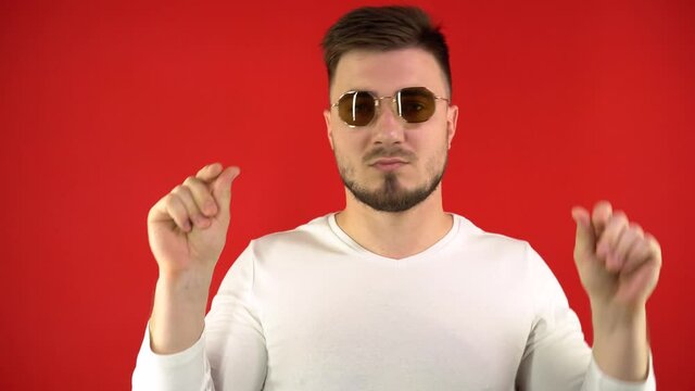 A seductive young man in trendy glasses dances stylishly and modestly against a bright red background. The concept of dancing and flirting. Studio footage, isolate, 4k.
