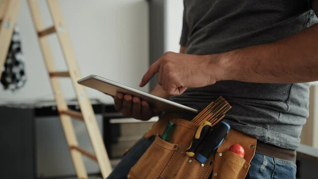 Video of carpenter with tool belt scrolling digital tablet. Shot with RED helium camera in 8K   