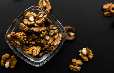 Walnut in a small plate with scattered shelled nuts which standing on a black surface. Walnuts is a healthy vegetarian protein nutritious food.