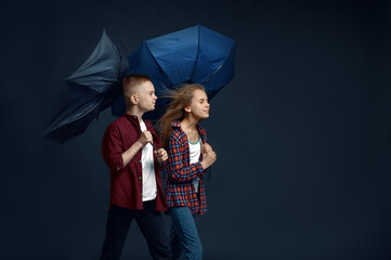 Boy and girl with umbrellas in studio, wind effect