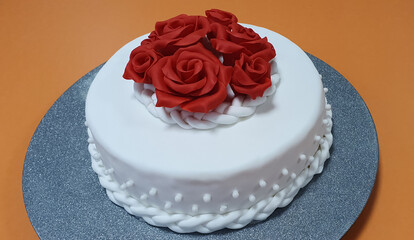 Obraz na płótnie Canvas Beautiful cake is covered with white sugarpaste and decorated with red roses