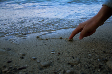 Hand drawing a heart in the sand