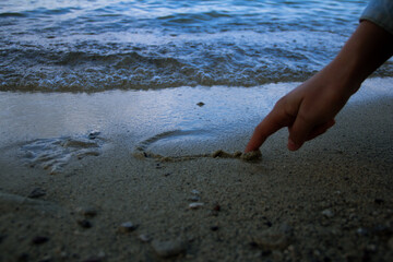 Fototapeta na wymiar Hand drawing a heart in the sand