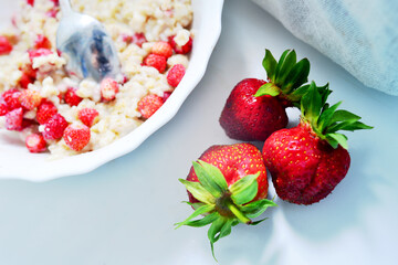 Red juicy strawberries with a plate of porridge on a light table. Healthy breakfast
