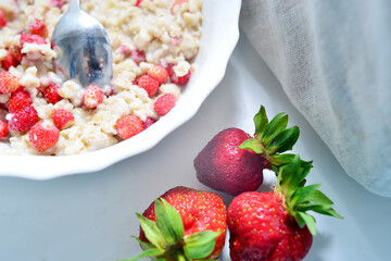 Red juicy strawberries with a plate of porridge on a light table. Healthy breakfast