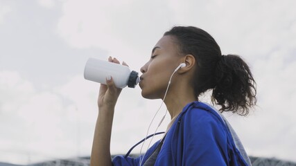 Afro-american runner woman Drinking Water or isotonic After Running. Portrait Fitness Woman Drinking Water From Bottle.