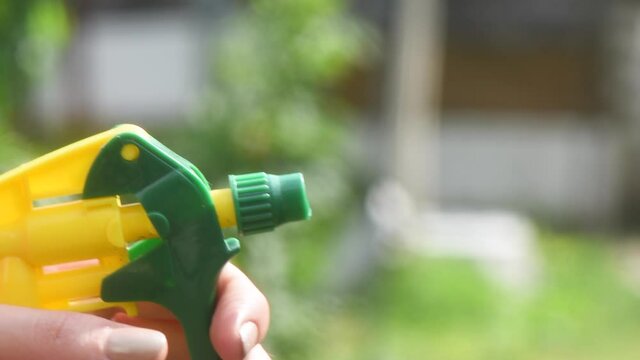 Female hand spray water drops with plastic spray in the garden.