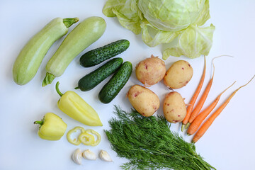 Cucumbers, cabbage, zucchini, peppers, garlic and herbs on a white background. View from above. Seasonal vegetables.