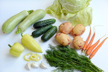 Close up of seasonal vegetables on a white background. Layout of cabbage, cucumbers, zucchini, peppers, carrots and dill.