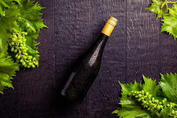 Weinflasche auf schwarzem Holz mit Weinblättern und Weintrauben mit Freiraum