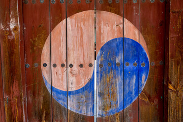 Taegeuk symbol painted on the wooden door with the flowers made of metal decoration.