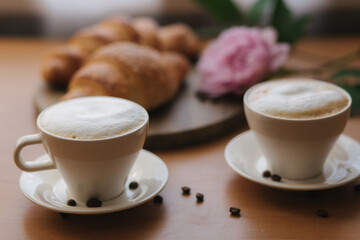 Vegan breakfast at home. Cappuccino with coconut milk and two empty vegan croissants. Morning with coffe. Pink peony flower on table