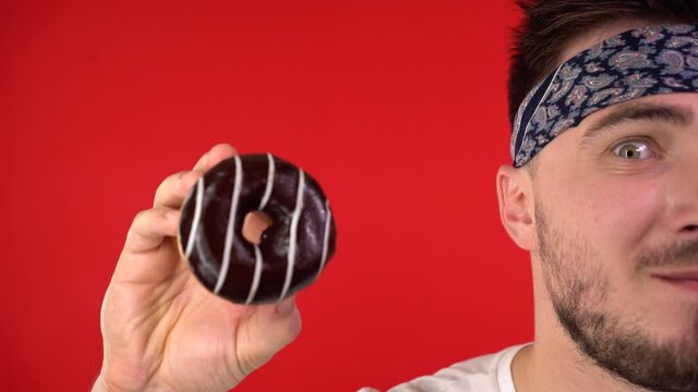 Close-up of a man with dark hair. A man holds a glazed donut in his hands, a man cannot help but wants to bite a donut. Sweet tooth man, addiction to sweets.
