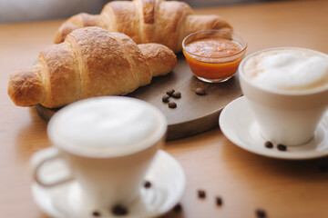 Morning coffee and croissant on wooden table. Cappuccino with freshly baked criossant ay home. Empty croissant on wooden board. Apricot jam