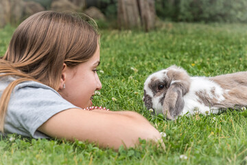Teenager girl and her rabbit lying in the green grass, looking at each other