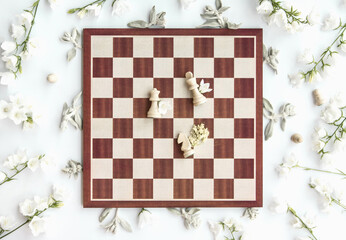 Styled wooden chess board scene with white queen, king and knight, white flowers, flatlay, view from above © ZM