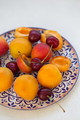 Apricots and cherries in a white ceramic plate with dark blue or