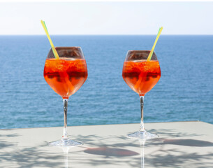 Close up of two glasses of chilled cocktail drinks with straws and  ice cubes on a table a sunny day at the beach. Blurry background of tranquil clean blue water and sky.