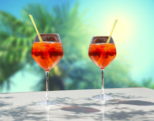 Close up of two glasses of chilled cocktail drinks with straws and ice cubes with backlit tropical palm trees and sun ray. Summer travel holidays vacation concept.