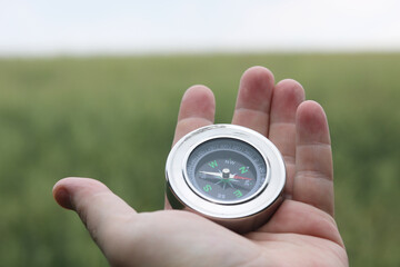 Old classic navigation compass in hand on natural background as symbol of tourism with compass, travel with compass and outdoor activities with compass