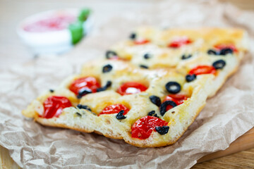 Focaccia with black olives, cherry tomatoes, rosemary and olive oil on a rustic wooden table. 