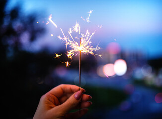 Woman hands holding sparkler, evening time.