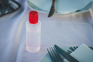 Bottle of hand sanitizer gel on restaurant table, between plates and cutlery. Dinner due coronavirus pandemia. Guests in restaurants can wash their hands before eating.