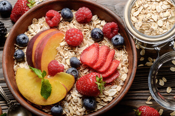 Flat lay of fruit healthy muesli with peaches strawberry almonds and blackberry in clay dish on wooden kitchen table