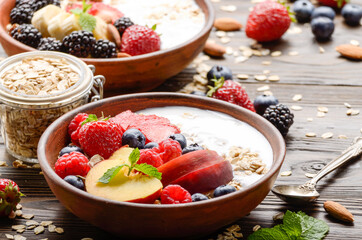 Fruit healthy muesli with peaches strawberry almonds and blackberry in clay dish with yogurt on wooden kitchen table