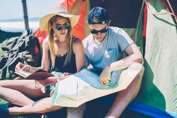 Obraz premium Young female tourist looking at her boyfriend pointing on location on map planning route together resting in tent, romantic couple in love explore nature together wanderlust on summer vacations