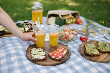 Woman take fresh orange juice on vegan picnic outdoors, Picnic on blue checkered blanket in park. Vegan food concept