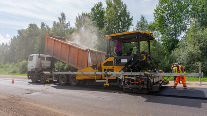 Truck loads asphalt into paver. Road repair works on the suburb highway