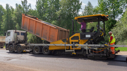 Truck loads asphalt into paver machine. Road repair works on the suburb highway