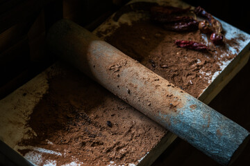 Grinding cacao beans with chili peppers to make chocolate by stone rolling pin on stone surface....