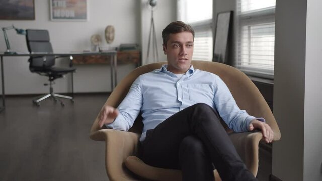 young stressed businessman sits in armchair in office. speaks emotionally, gesticulates actively. looks troubled and indignant, because of problems. has consultation with psychologist. looks in camera