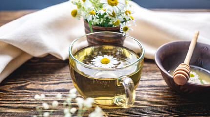 Transparent сup of hot chamomile tea and honey. Concept of a healthy soothing herbal drink after a...