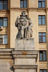 Obraz premium MOSCOW / RUSSIA - 20/04/2019 soviet communist stone sculpture of a strong soldier sitting with a gun (sculptors - Baburin, Nikogosyan, Anikushin). Kudrinskaya Square Building (Aviators' House) facade