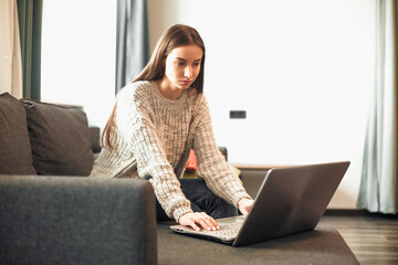 Young woman with modern laptop sitting on sofa at home