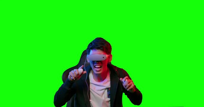Excited young asian teen gamer wearing virtual reality glasses and holding controllers having fun enjoy playing motion sensing interaction vr game in colourful UV lighting over green screen background