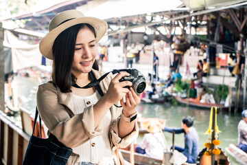 asia female tourists wearing hat holding camera and smartphone take photo vlog live. Beautiful woman take taxi boat visiting Damnoen Saduak floating market,Ratchaburi.