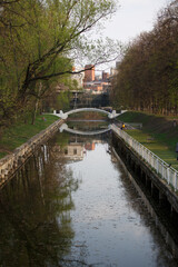 MOSCOW / RUSSIA - 20/04/2019 narrow water Canal in the Krasnaya Presnya park with people relaxing at the quay, a bridge and buildings, tall trees with branches, green leaves in the background