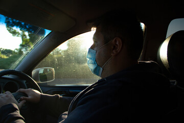 Fototapeta na wymiar A man in a car driving in a medical mask from a coved - 19