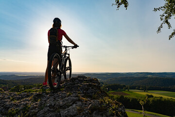 Fototapeta na wymiar young woman admiring the awesome view over Frankonian Switzerland, during a mountain bike trip during golden hour in the evening
