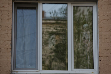 Close up day shot of a human body skeleton figure standing in the corner of a white window frame scaring the people passing by