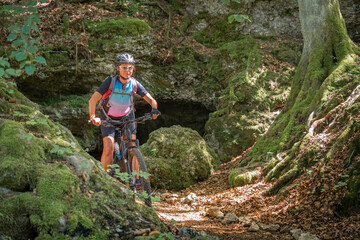 Obraz premium pretty senior woman underway on her electric mountain bike on a rocky forest trail in Franconian Switzerland, Bavaria, Germany
