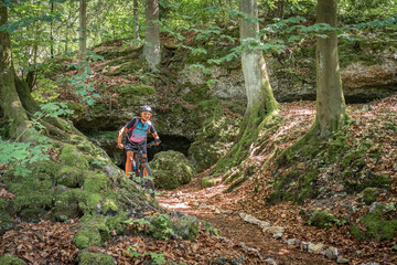 Fototapeta premium pretty senior woman underway on her electric mountain bike on a rocky forest trail in Franconian Switzerland, Bavaria, Germany