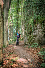Naklejka premium pretty senior woman underway on her electric mountain bike on a rocky forest trail in Franconian Switzerland, Bavaria, Germany