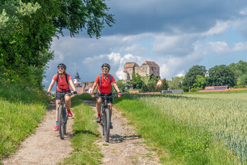 Obraz premium grandmother and granddaughter riding their mountain bikes in front of the awesome skyline of Hiltpoltstein in Frankonian Switzerland, Bavaria, Germany