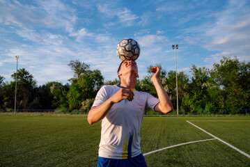 Young male soccer player juggles a ball with his head on a soccer field